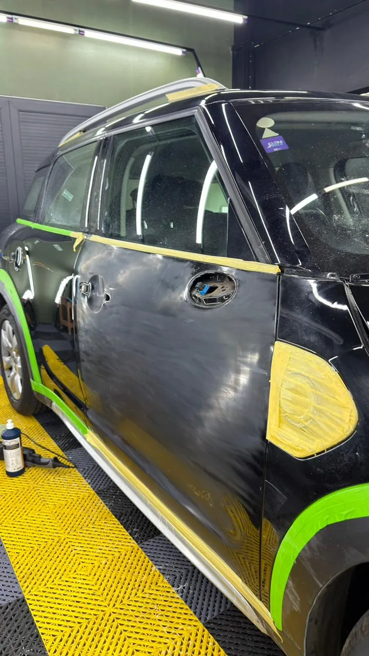 Close-up of the Mini’s door and wheel arch, masked with tape before work begins.